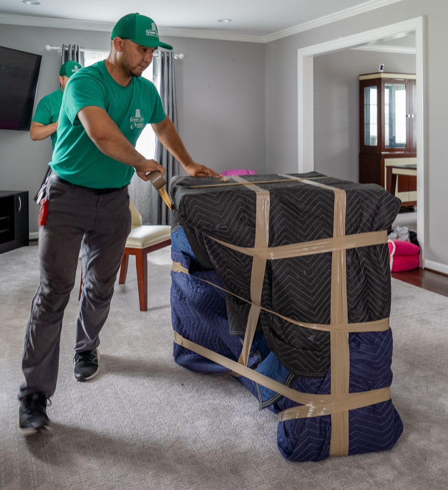 Movers wrapping a piece of furniture with protective padding and tape.