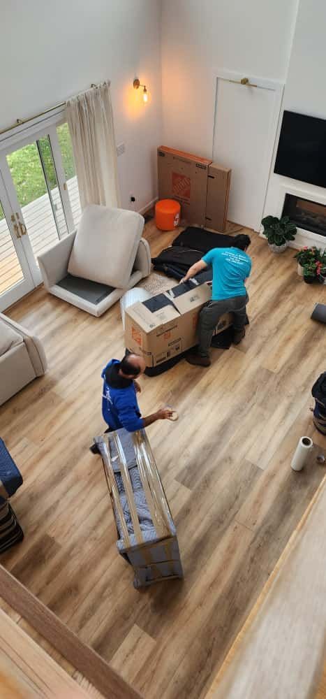 Two movers in blue shirts moving furniture inside a light-filled room.