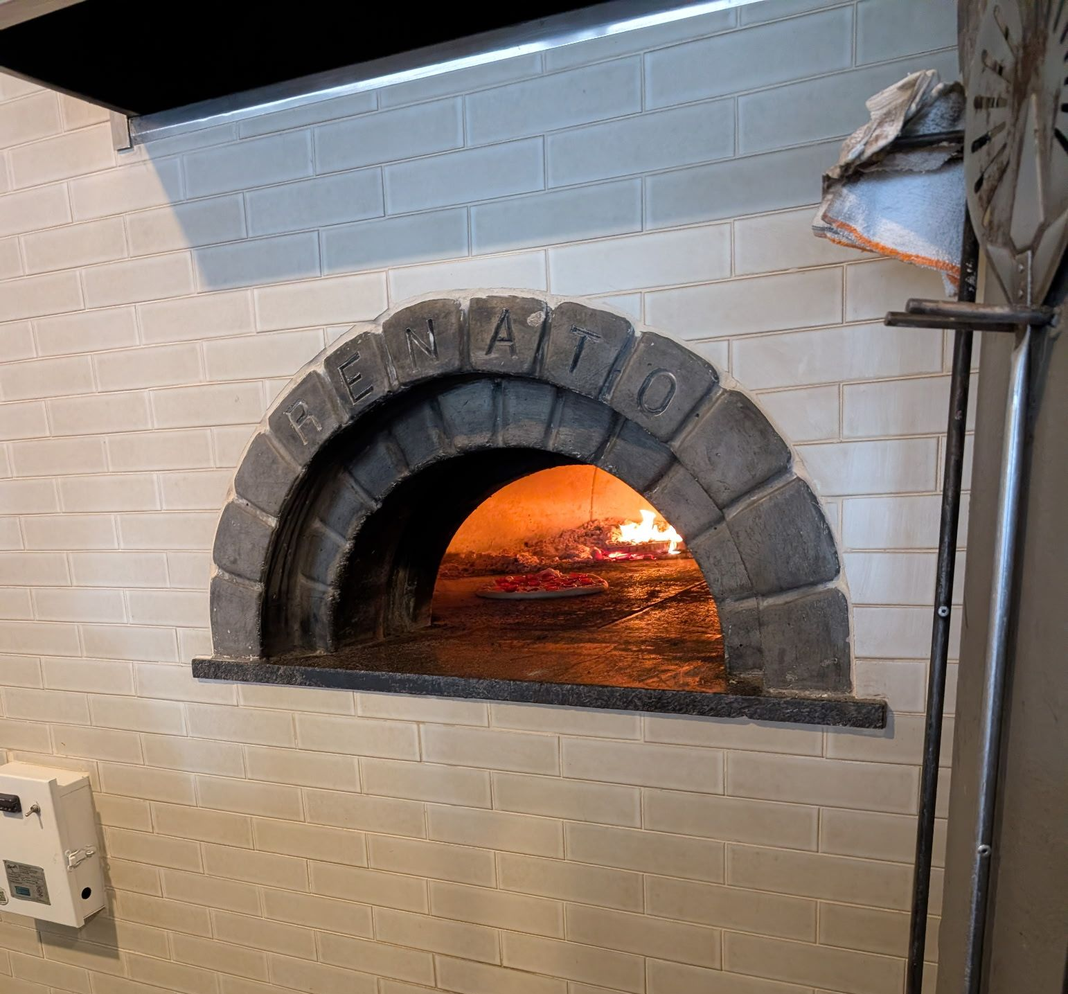 Wood-fired pizza oven with flames inside. The arch is labeled