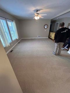 Empty living room with patterned carpet, ceiling fan, and a person standing near the right wall.