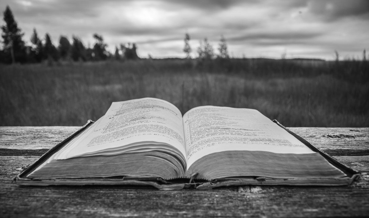 A black and white photo of an open bible on a wooden table.