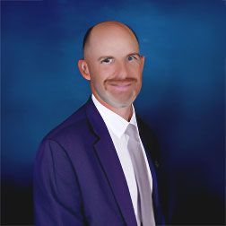 A man in a blue suit and tie is smiling for the camera.