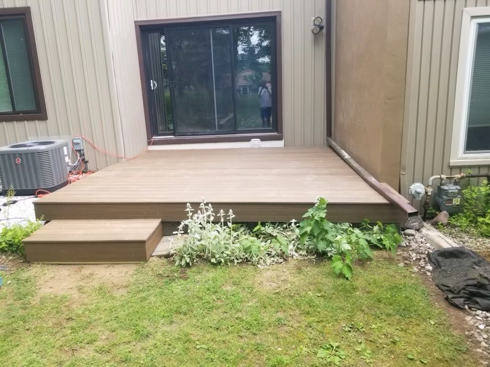 A brown composite deck with steps outside a beige house, next to a grassy yard.