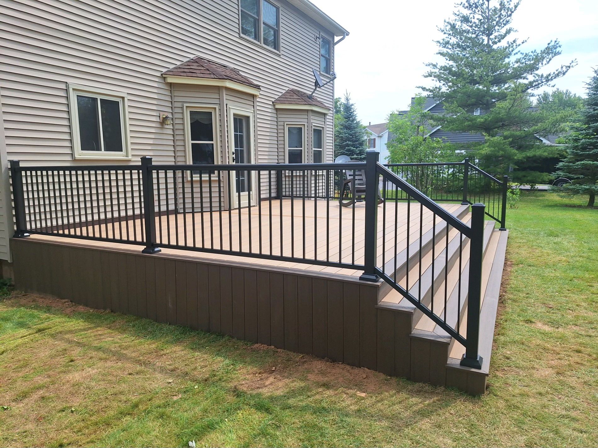 Composite deck with black railing attached to a house with beige siding, situated in a grassy backyard.