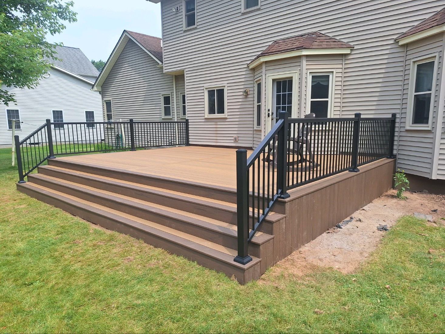 A large deck with stairs and a railing in front of a house.