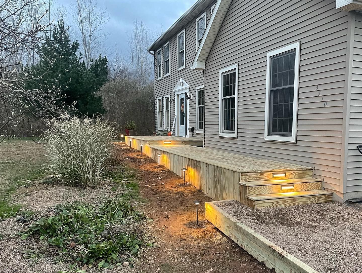 Exterior of a two-story house with a wooden walkway and steps, illuminated by small lights.