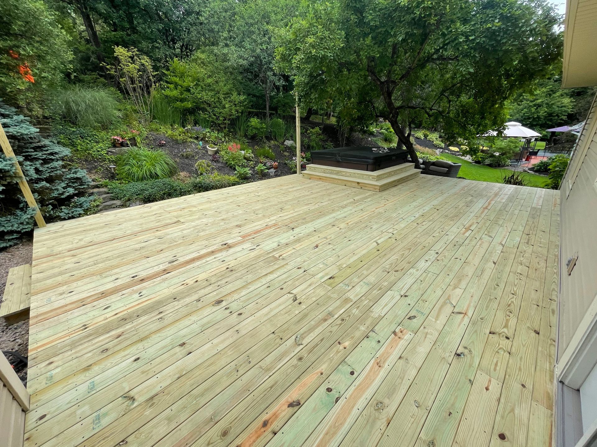 Wooden deck in a backyard, with tiered planter box, lush greenery, and trees.
