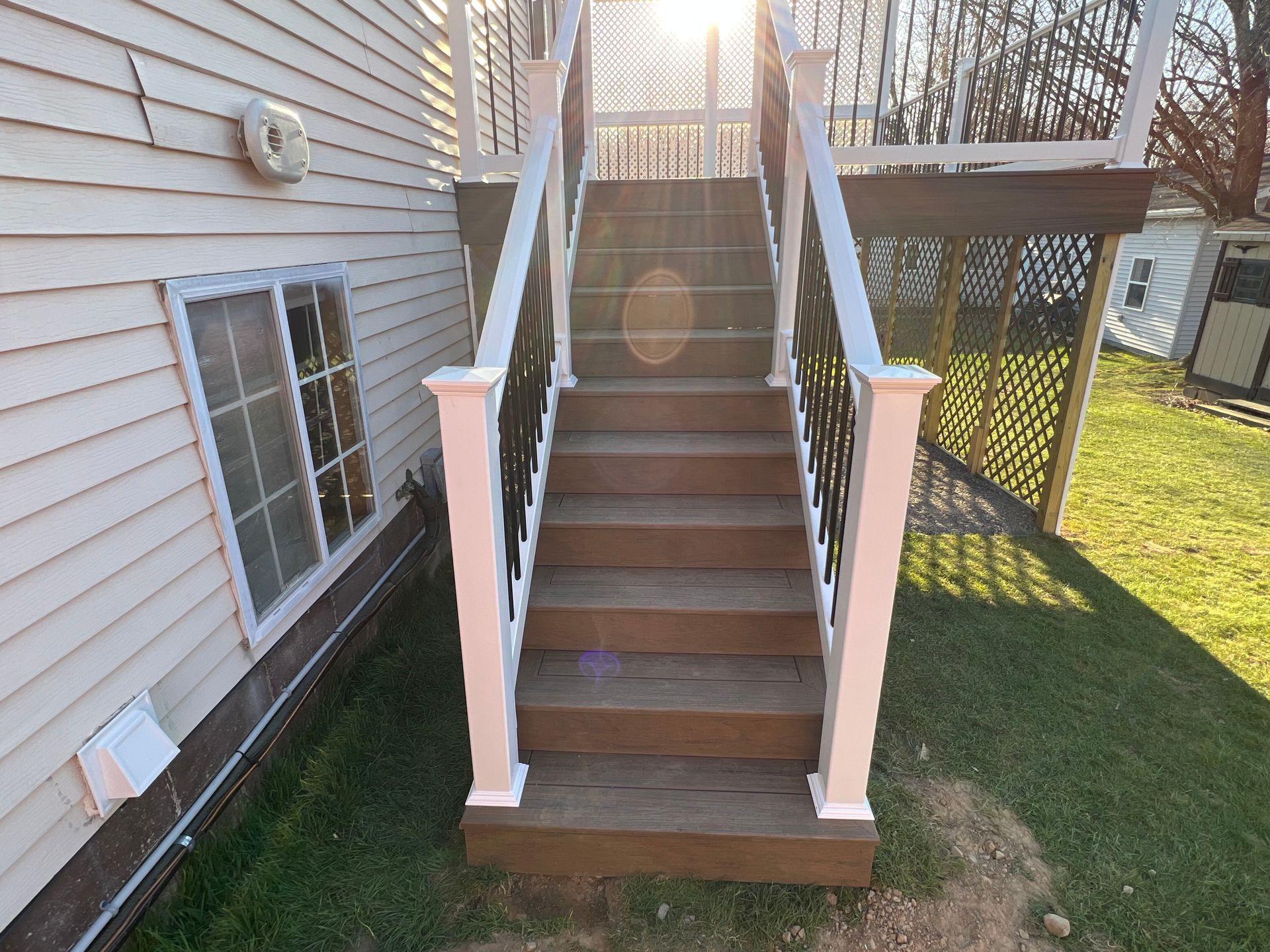 Wooden stairs leading up to a deck, white railing, black spindles, sunlight shining.