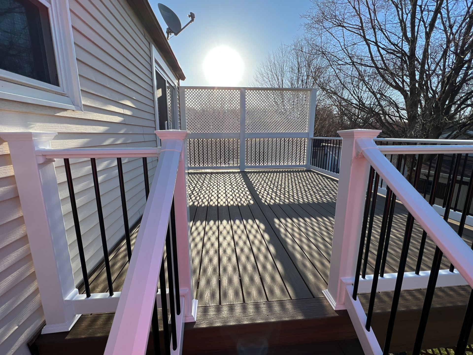 Wooden deck with white railing, black spindles, and a decorative screen; sun shining.