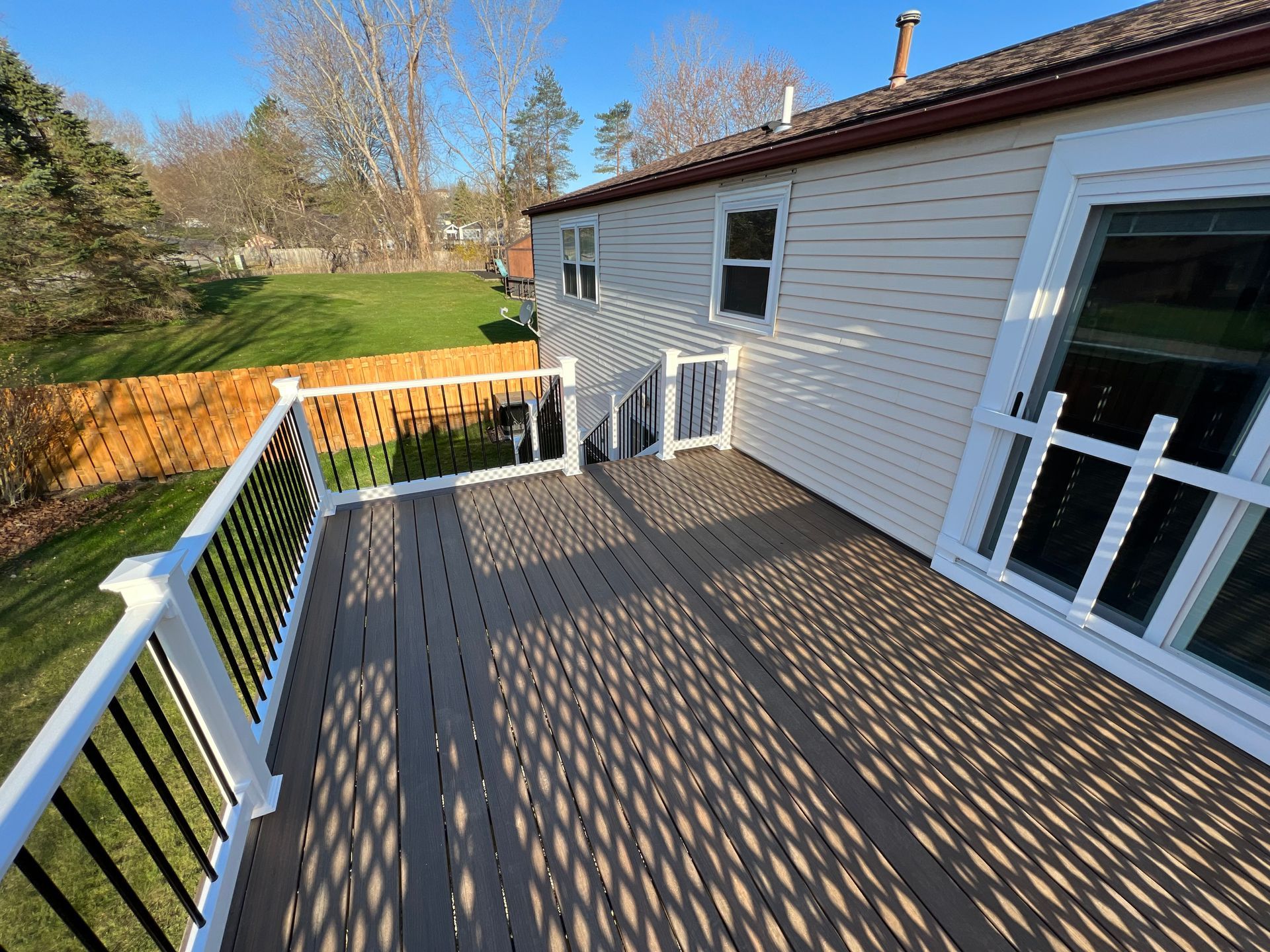 A large deck with a white railing and a white house in the background.