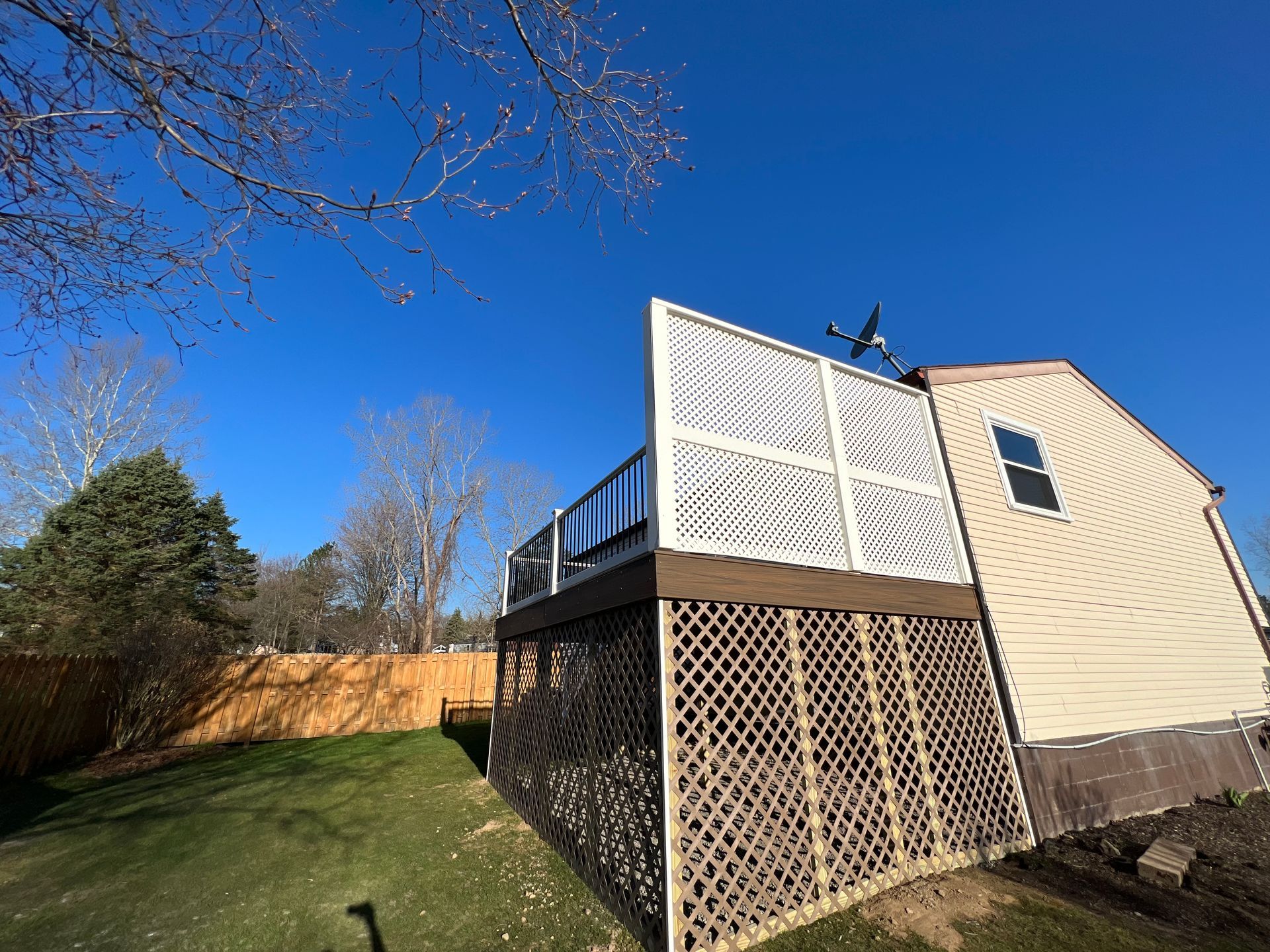 A deck with white decorative panels and lattice skirting next to a house under a blue sky.
