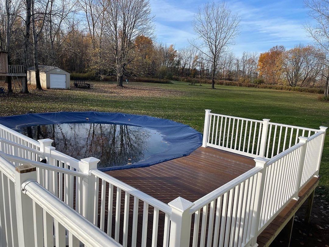 A deck with a white railing and a pool in the background.