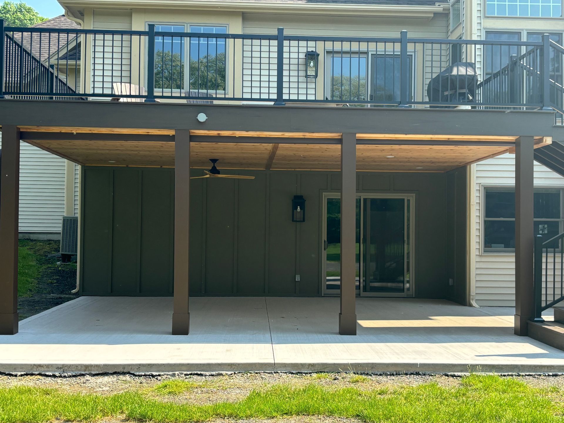 Covered patio under a deck, featuring concrete floor, brown posts, and a green wall.
