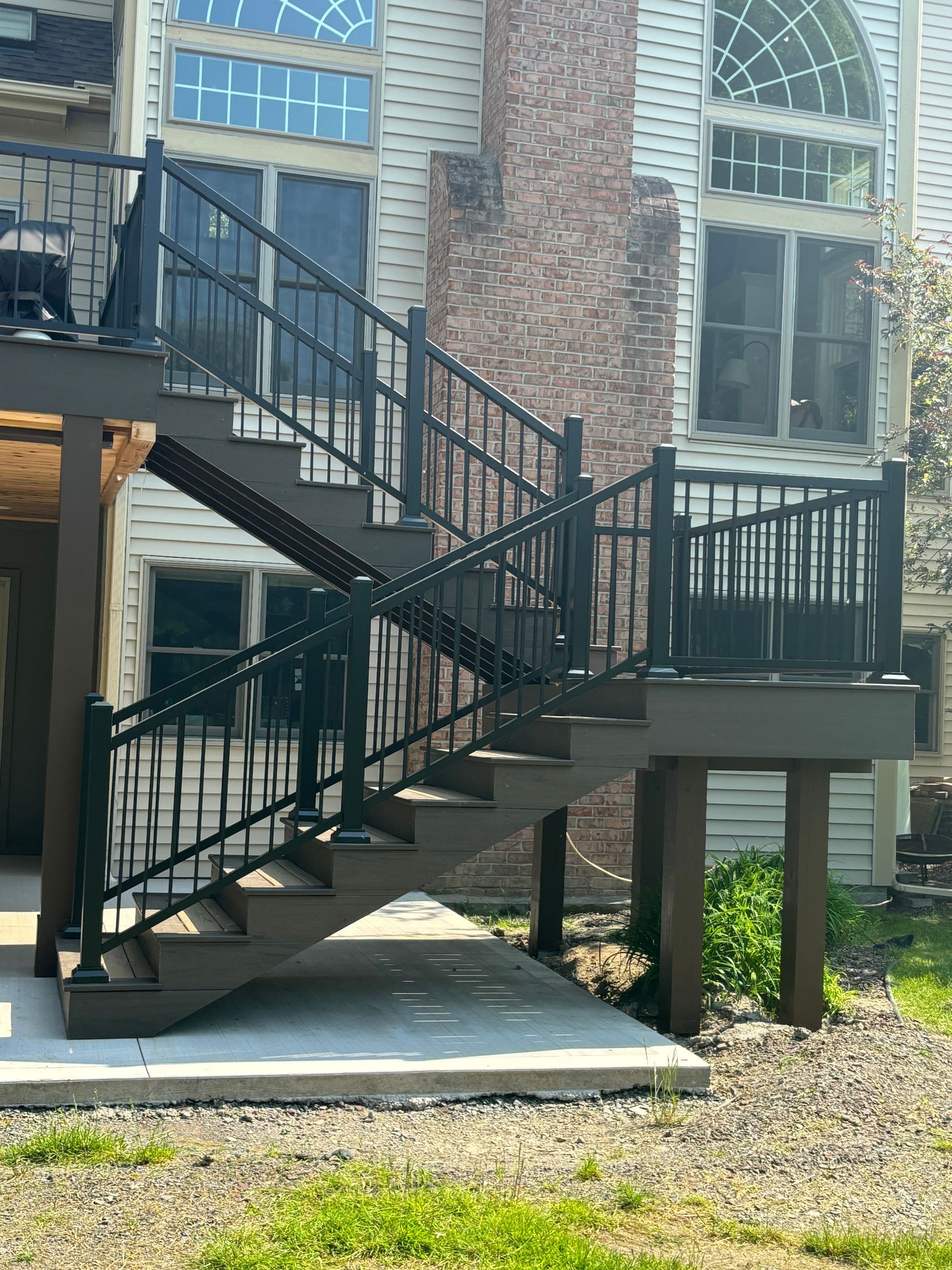 Outdoor staircase with black railings leading from a deck to a concrete patio.