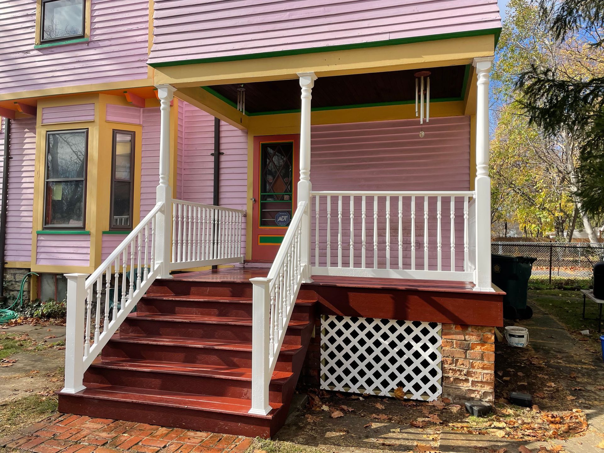 Pink house with white porch, red stairs, and a screen door.