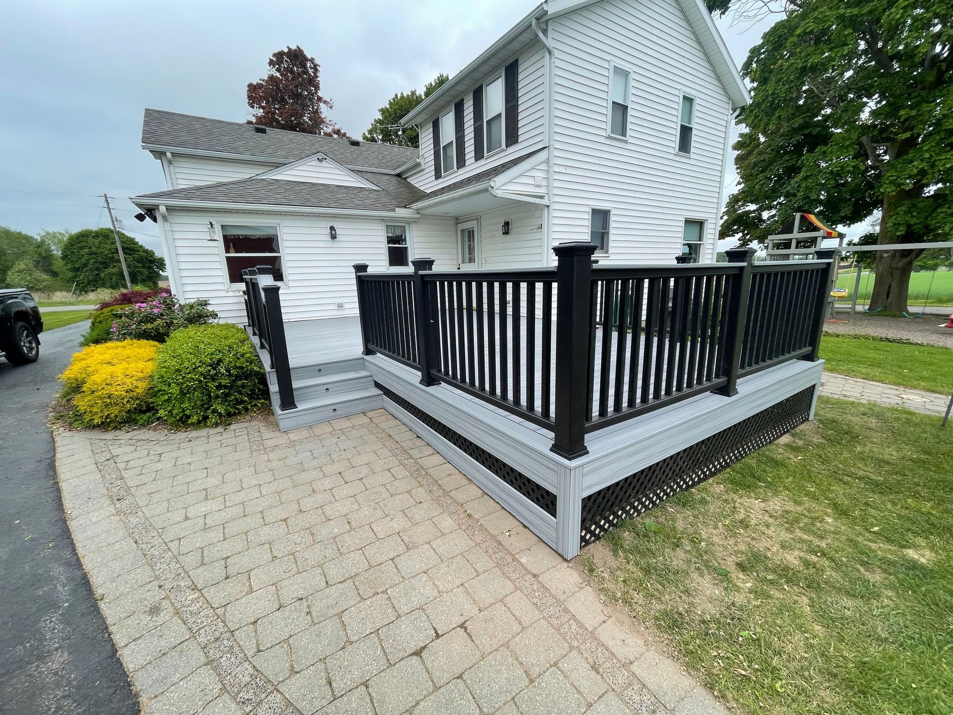 A white house with a black deck and stairs in front of it.