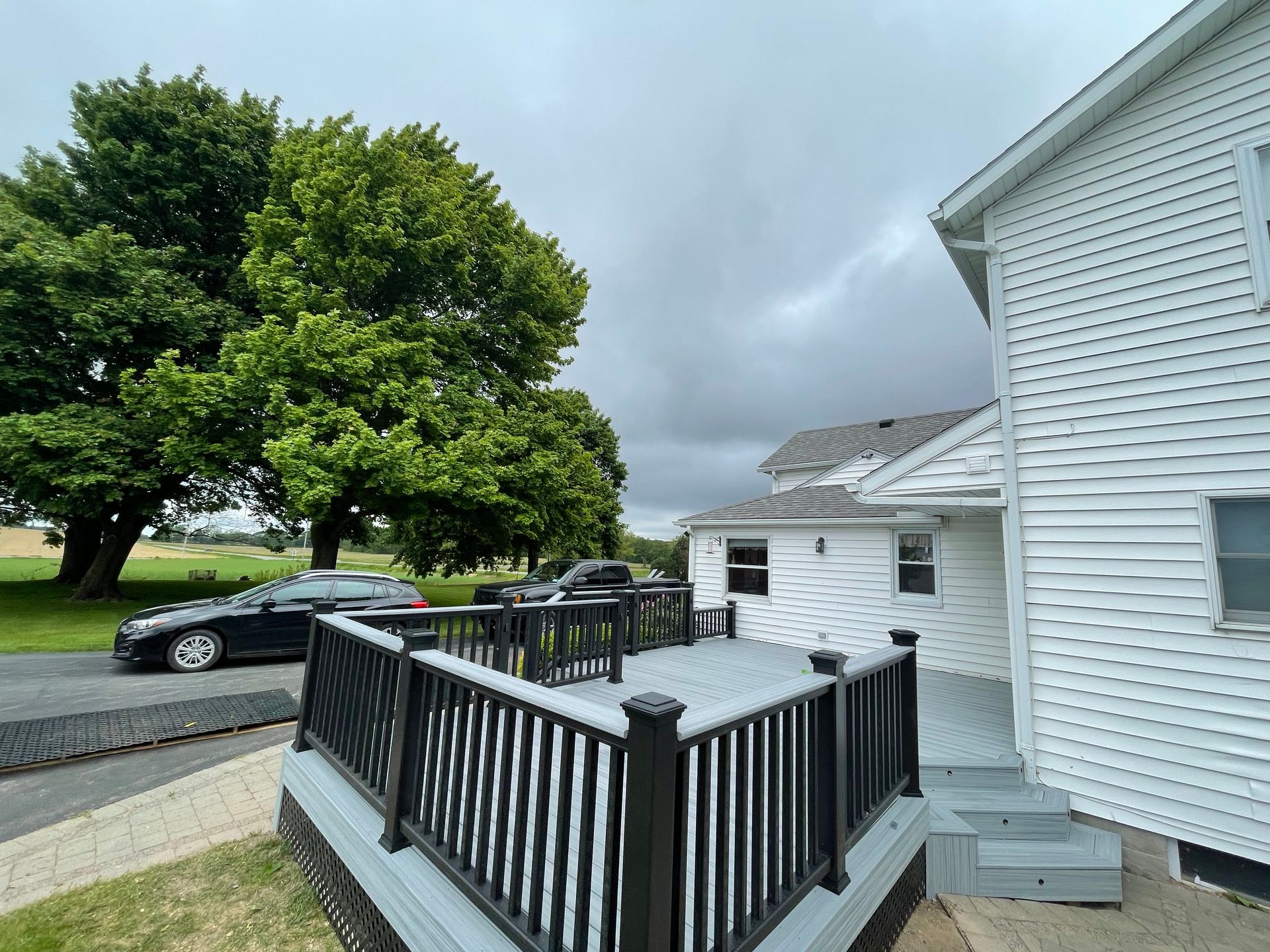A white house with a black deck and a black car parked in front of it.