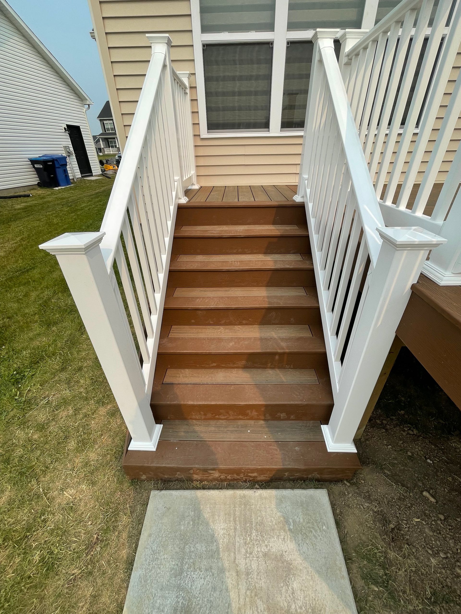 Wooden stairs with white railing lead up to a deck and a light-colored house.