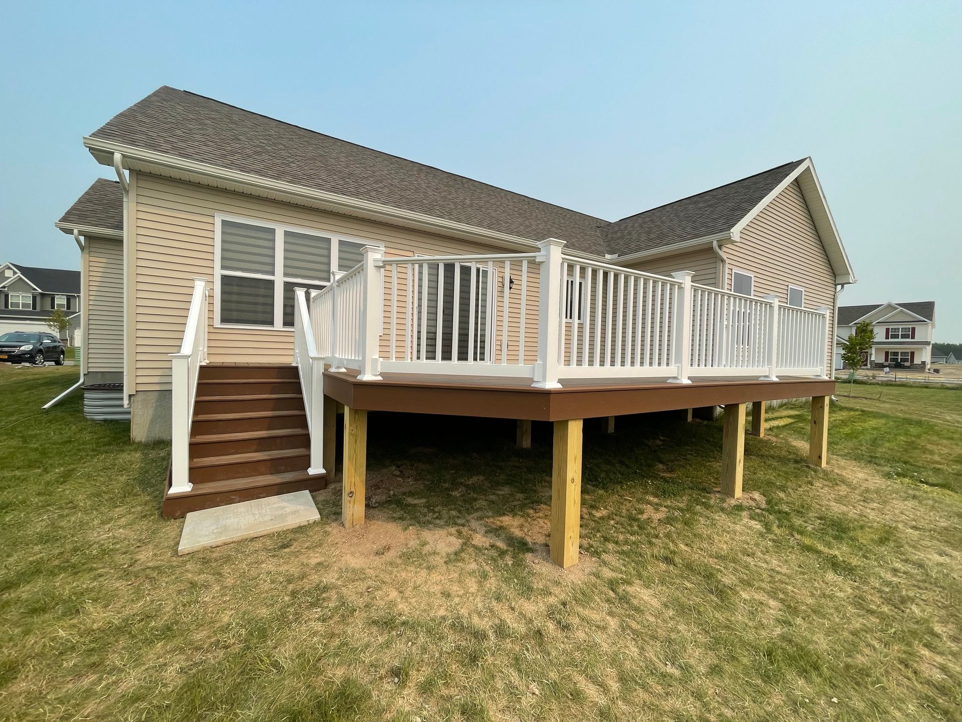 Deck with brown steps and white railing attached to a beige house.