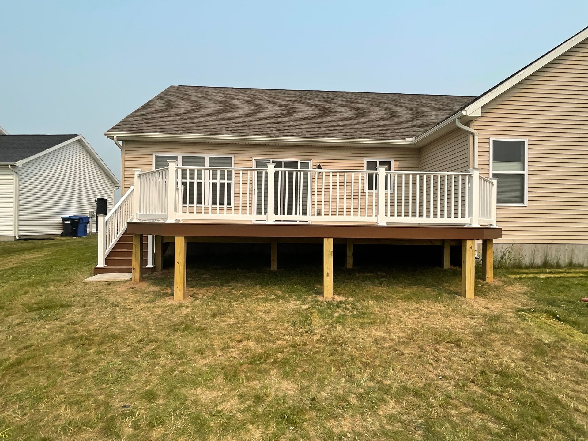 Deck attached to a house with white railing and brown deck boards, supported by wooden posts, on a grassy yard.