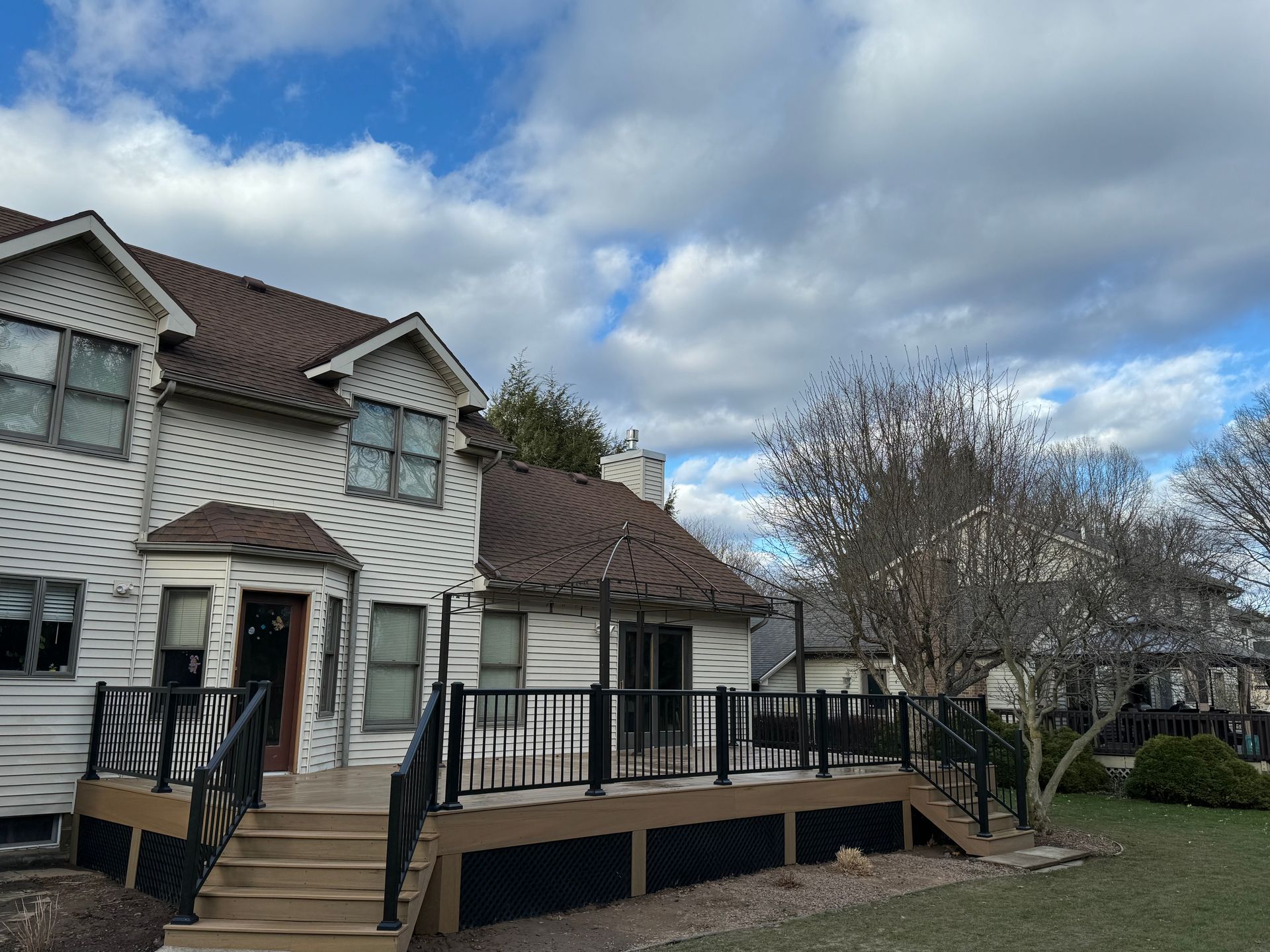 A two-story house with a wooden deck and black railings under a cloudy sky.
