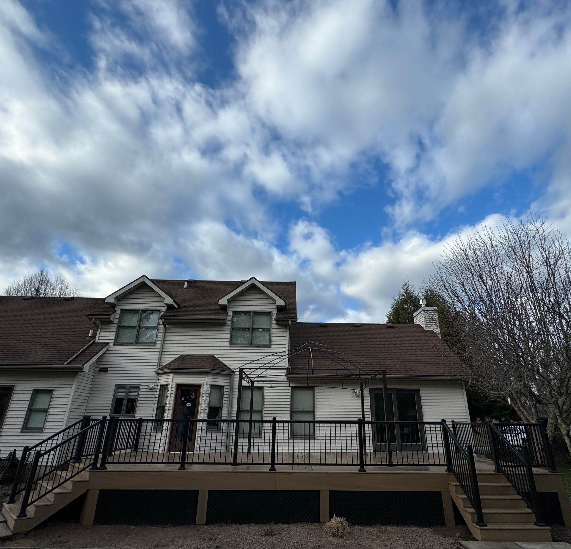 White house with brown roof and deck, under a partly cloudy blue sky.