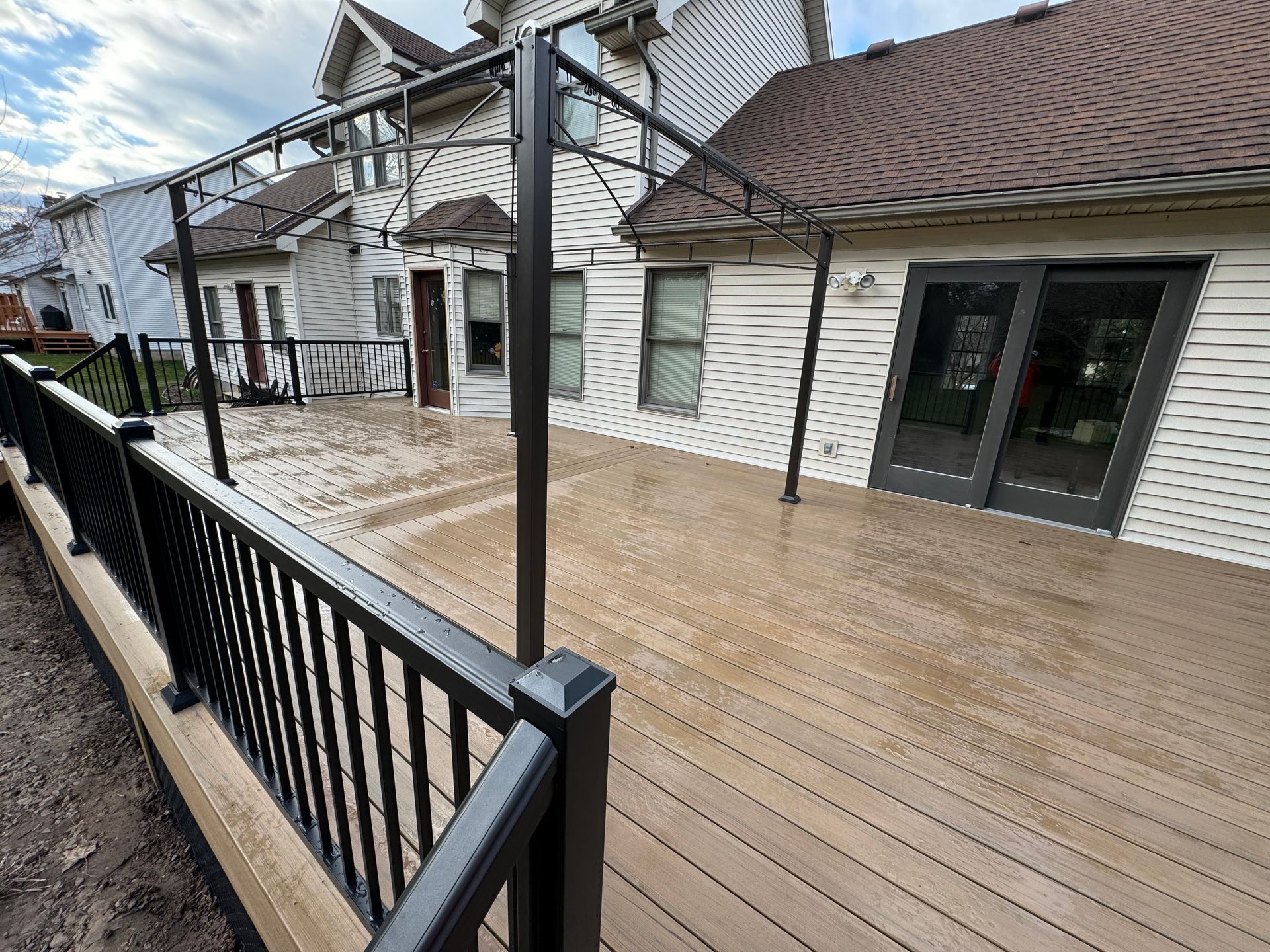 A spacious deck with black railing and pergola, attached to a white house with brown roof.