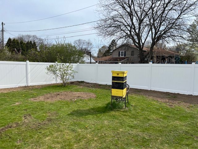 A backyard with a white fence and a yellow chair in the grass.