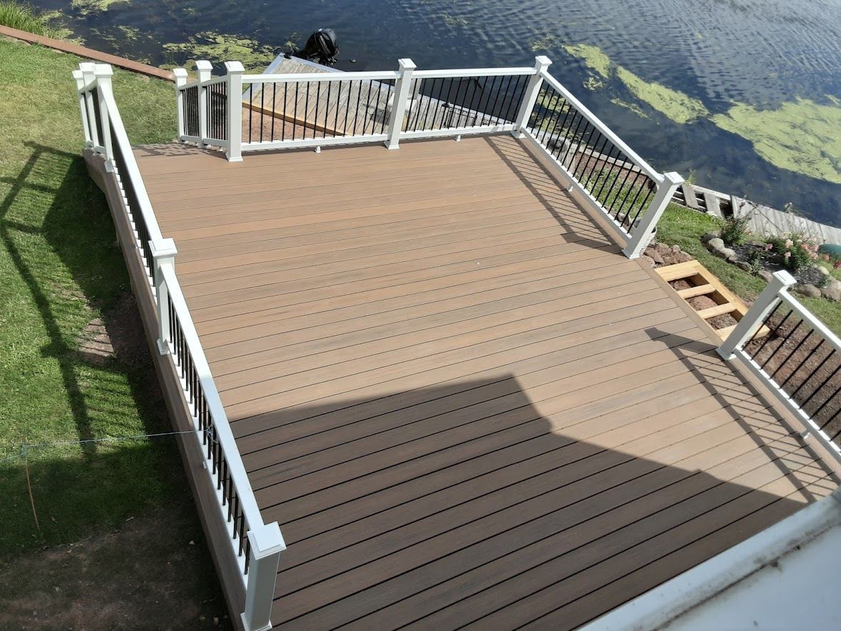 Wooden deck with white railing overlooking a body of water and hillside.