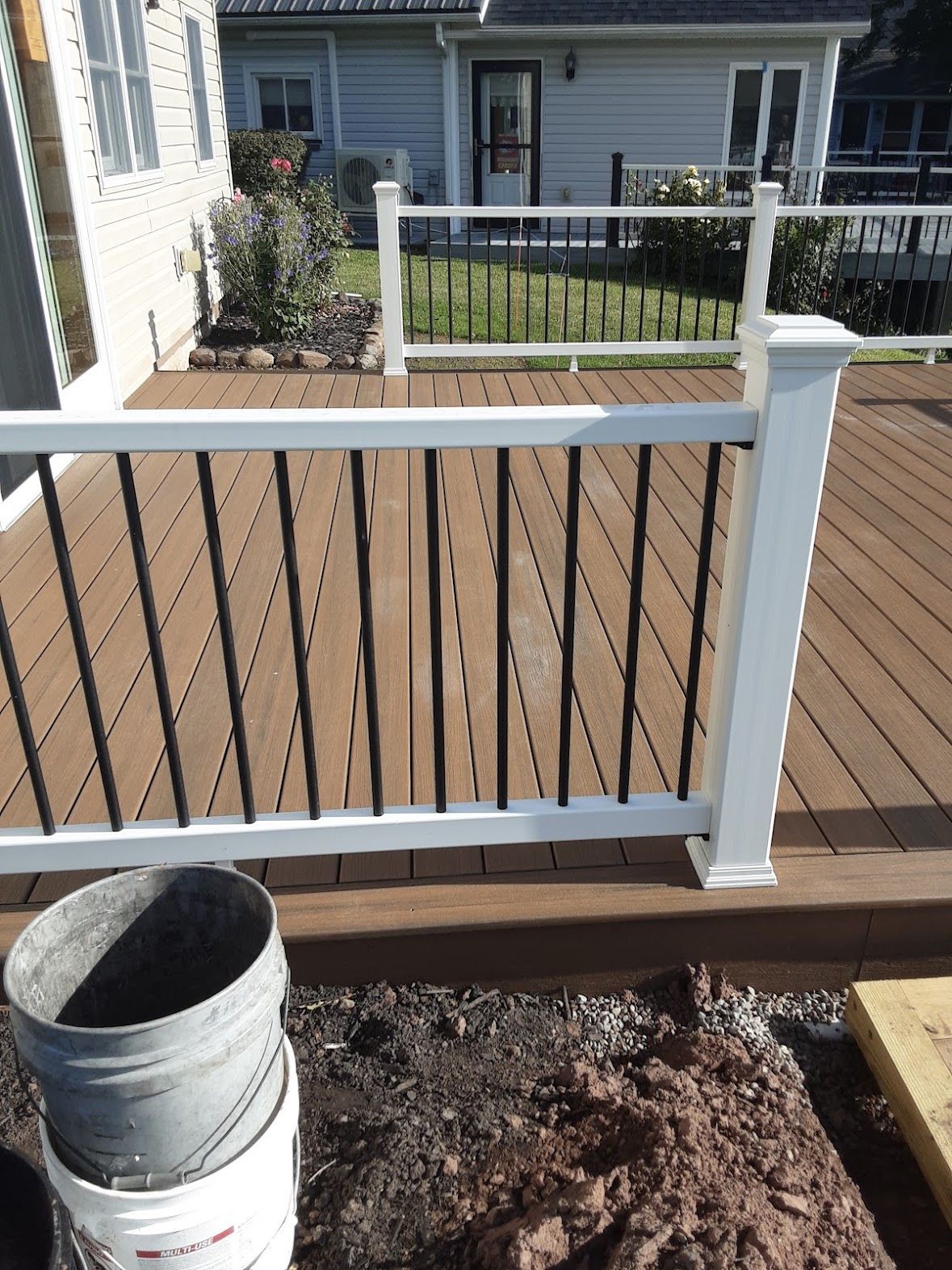A deck with a white railing and a bucket on the ground
