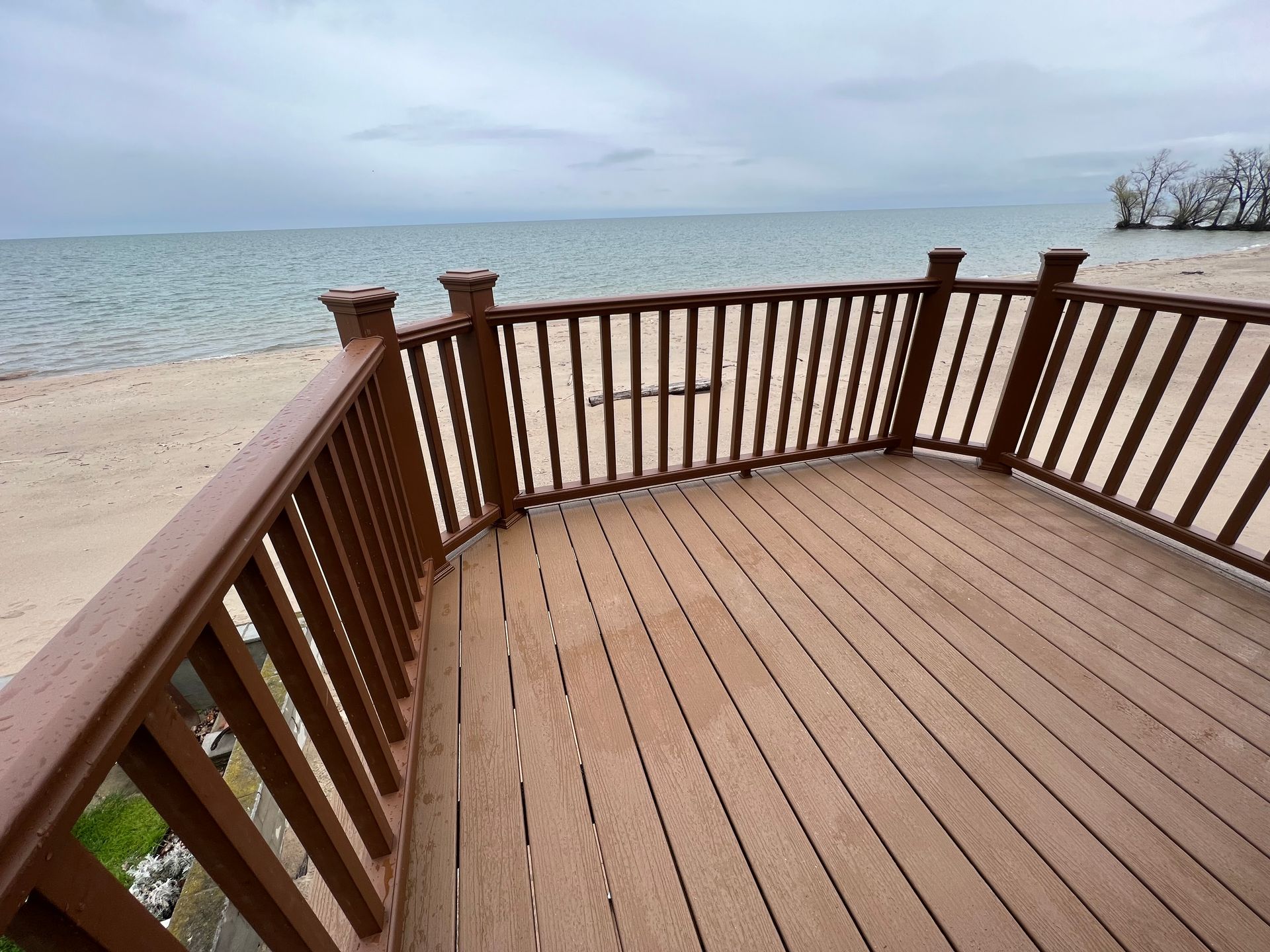 Wooden deck overlooking a sandy beach and ocean under a cloudy sky.
