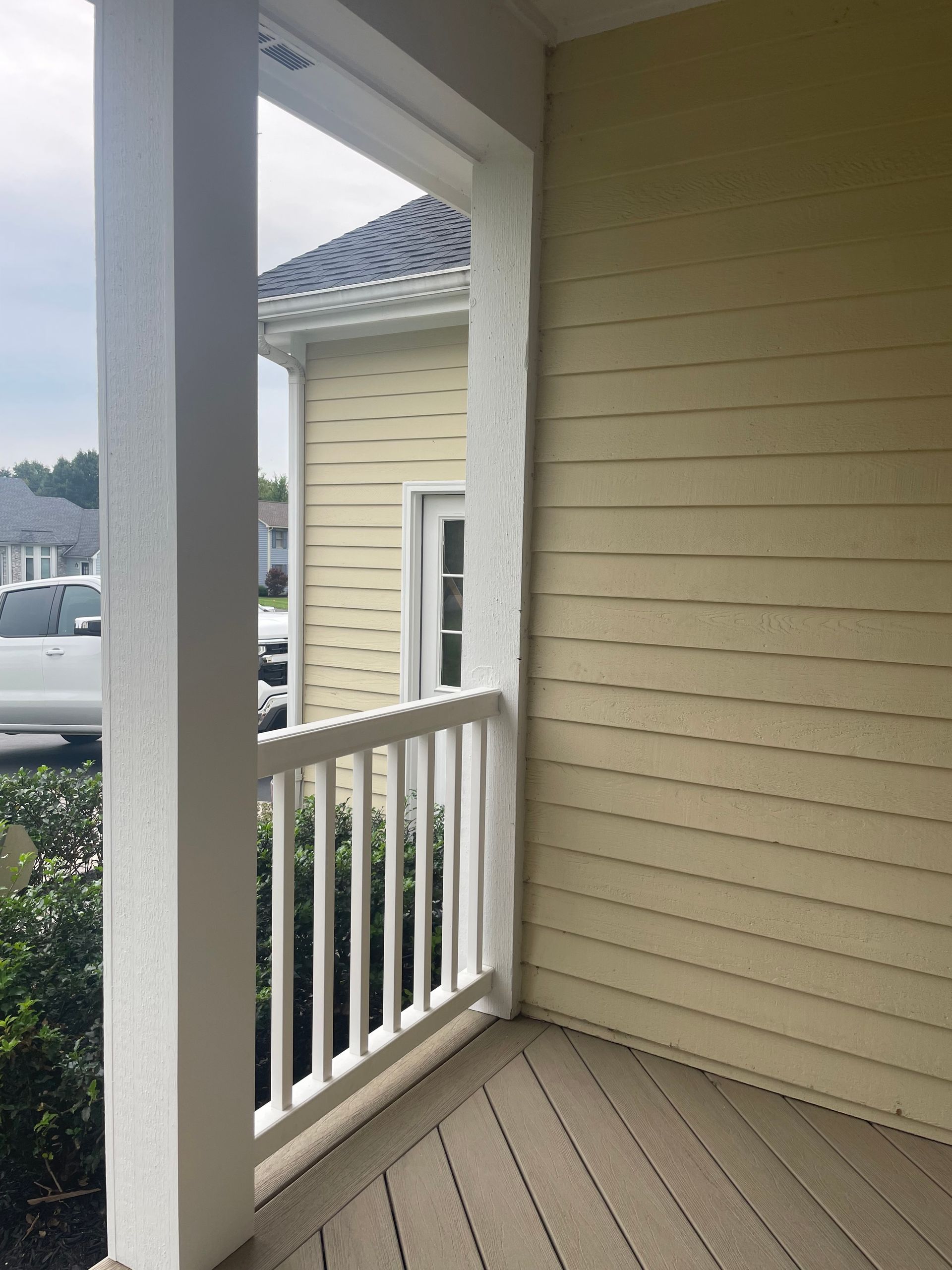 Porch with white railing, yellow siding, and a view of a building and parked cars.