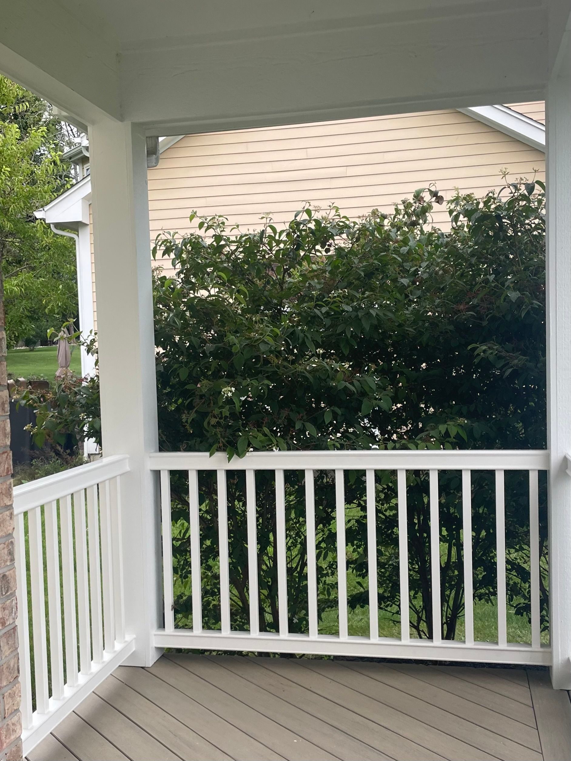 White porch with railing and view of green trees and house.