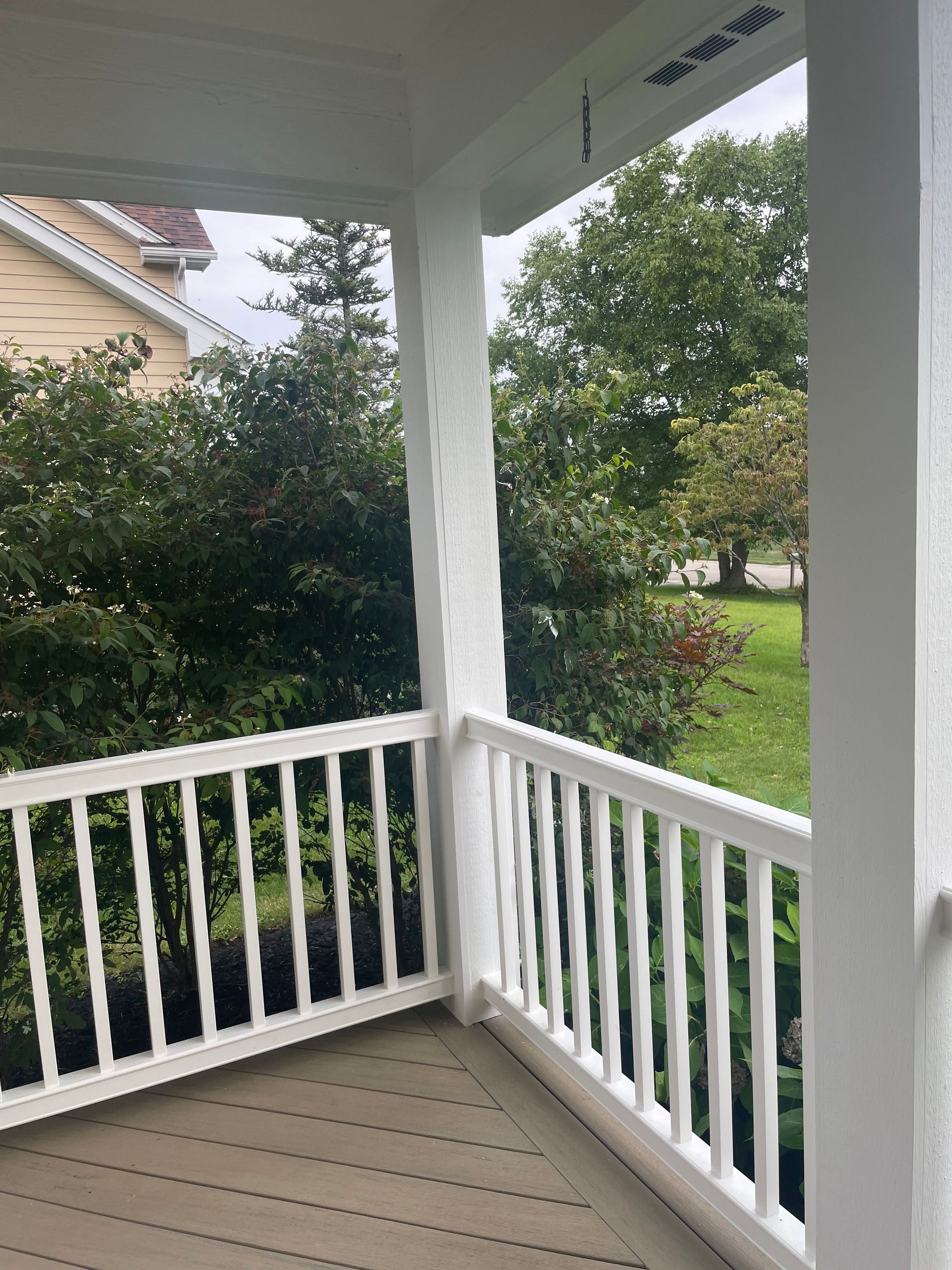White porch with railing overlooking trees and a grassy yard.
