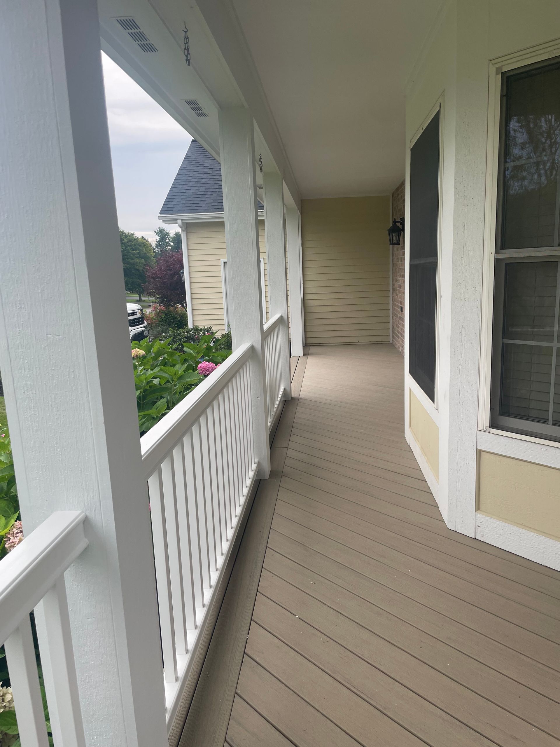 Covered porch with white columns, railing, and tan flooring. Overcast day.
