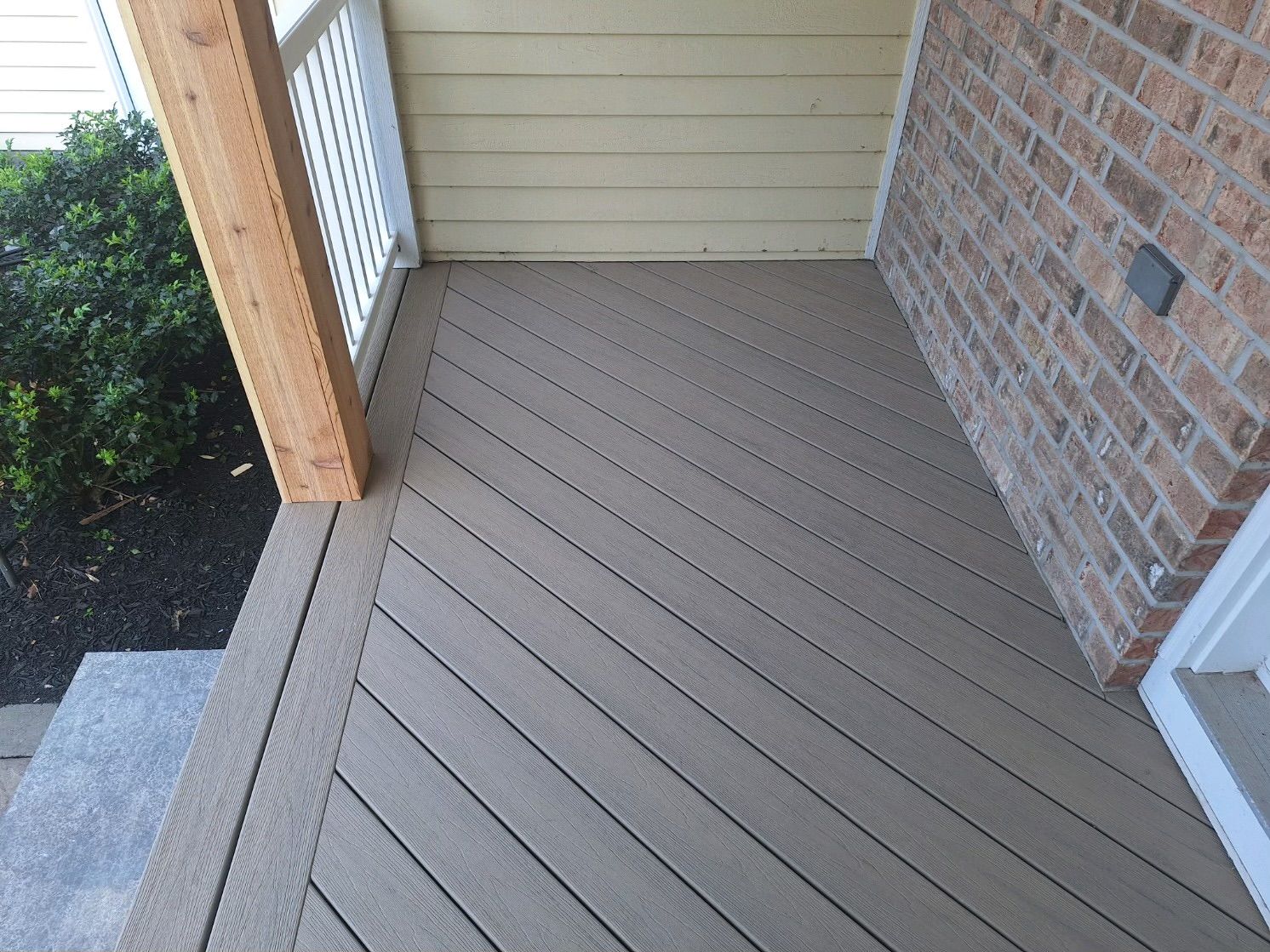 Beige composite deck with angled boards, brick wall, and wooden support.