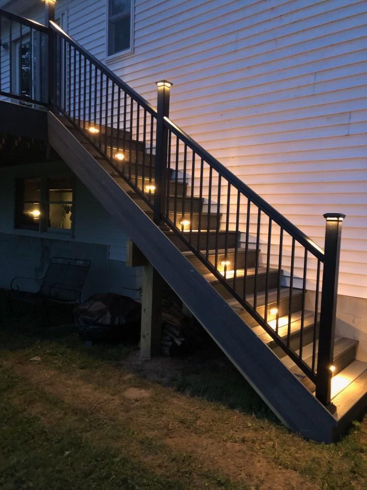 Outdoor staircase with dark railing and step lights leading to a deck on a house at night.