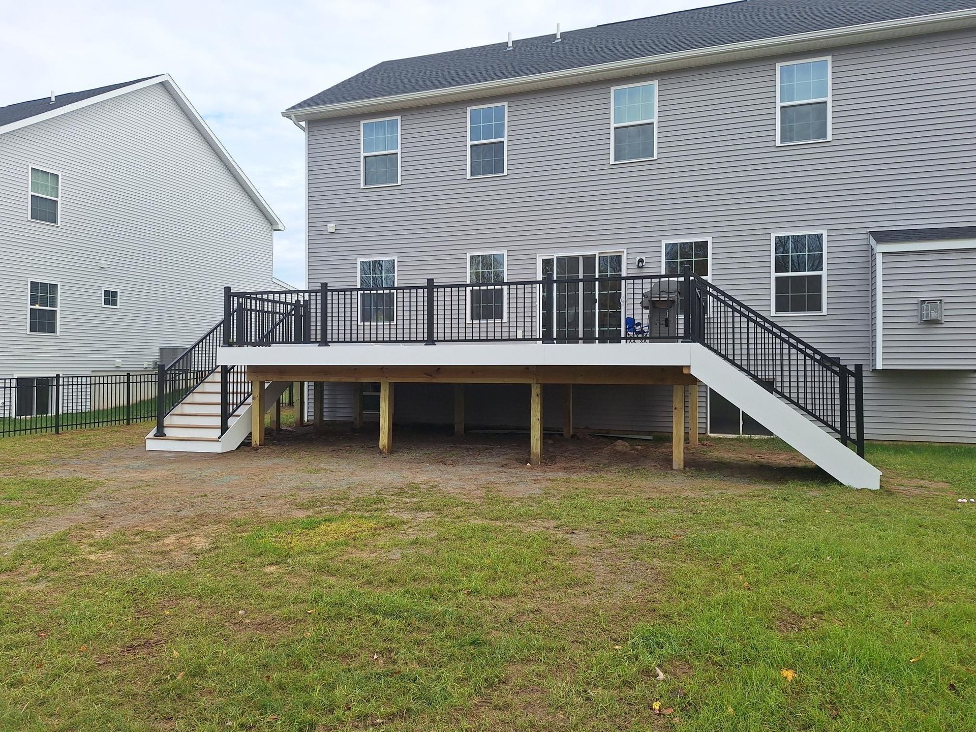 A two-story house with a large deck. Deck has black railing and stairs, gray siding, and a grassy yard.