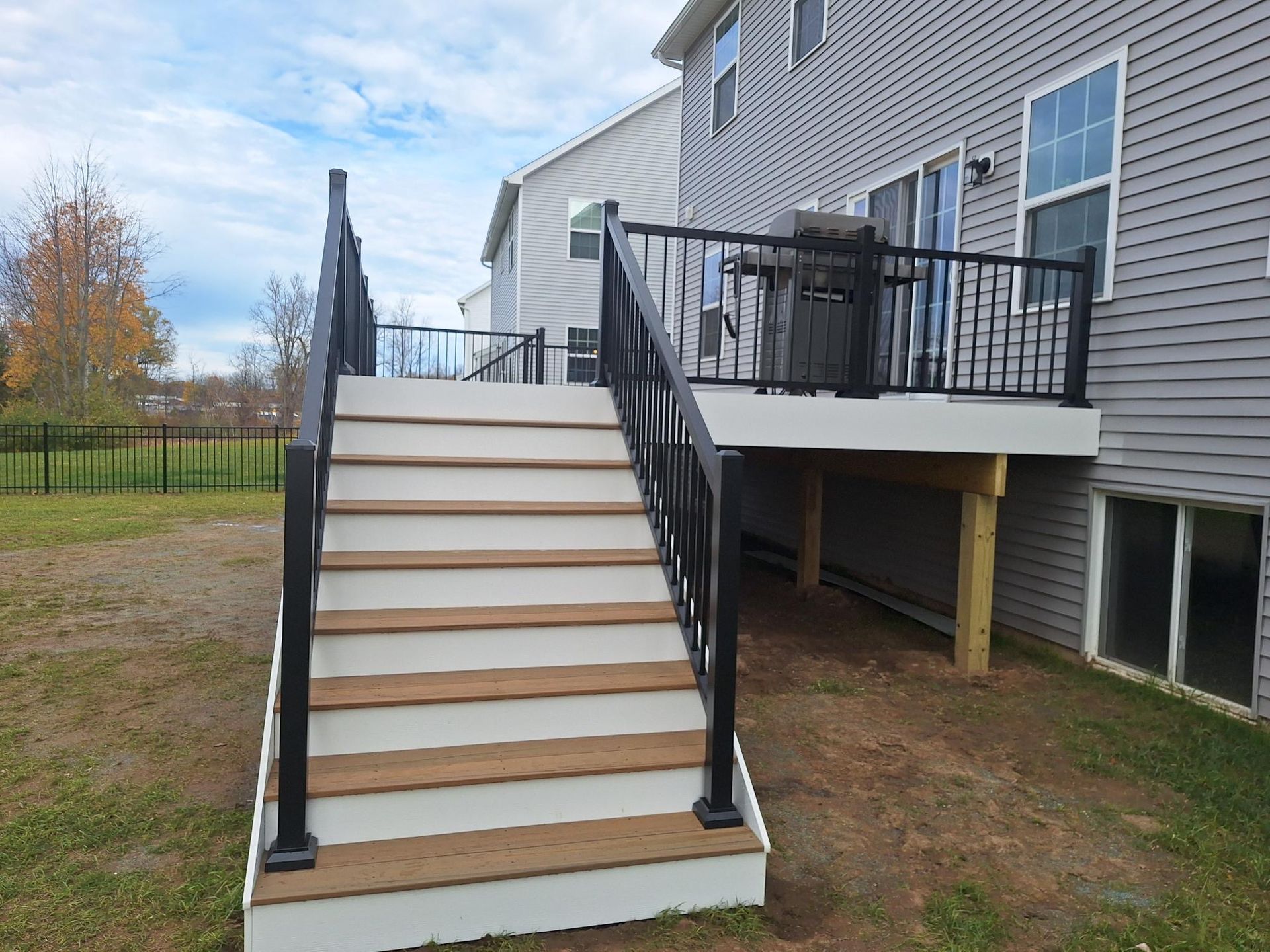 A composite deck with stairs and black railings attached to a two-story house. Brown steps and white trim.