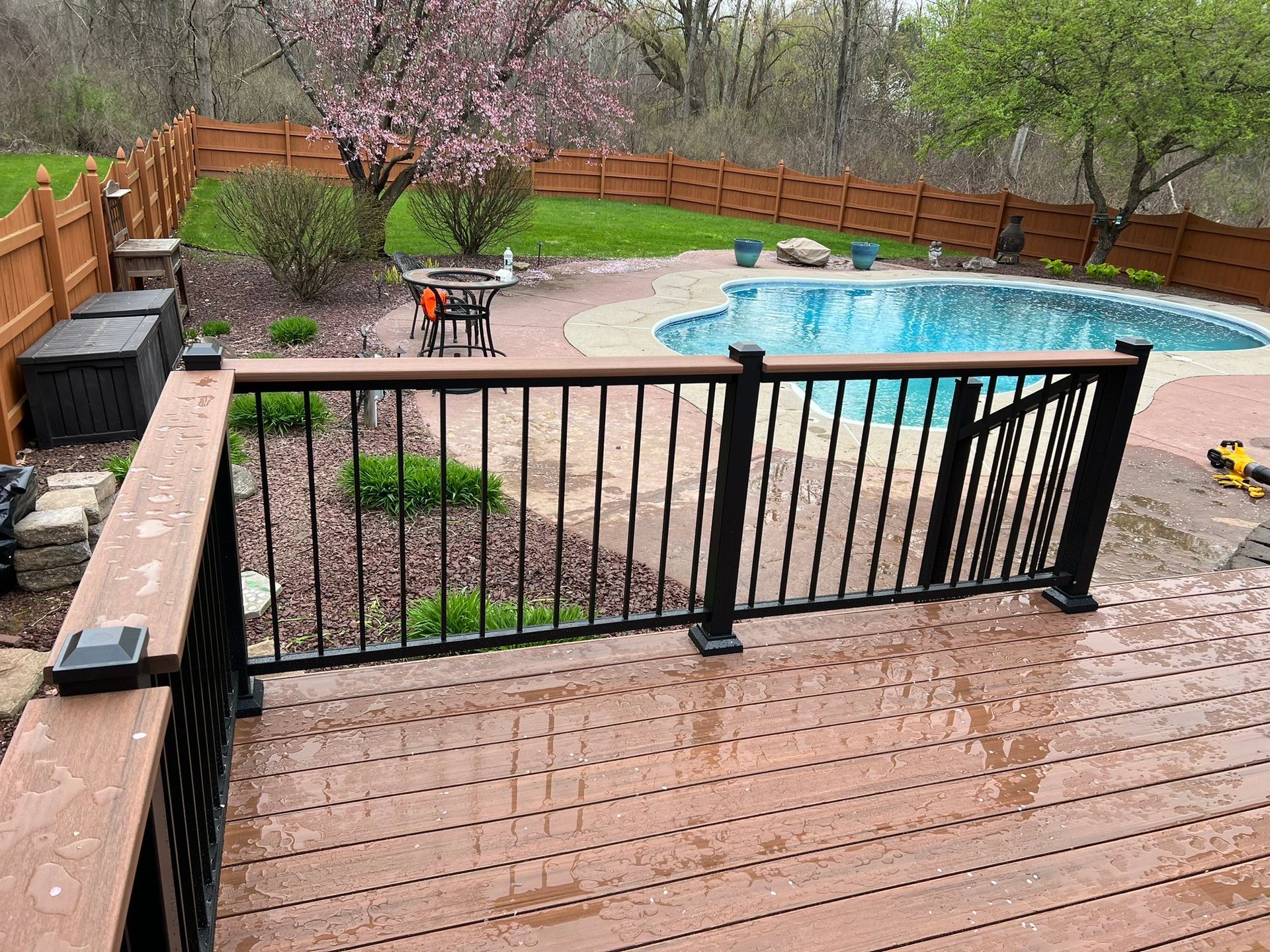 A wooden deck with a black railing overlooking a swimming pool.