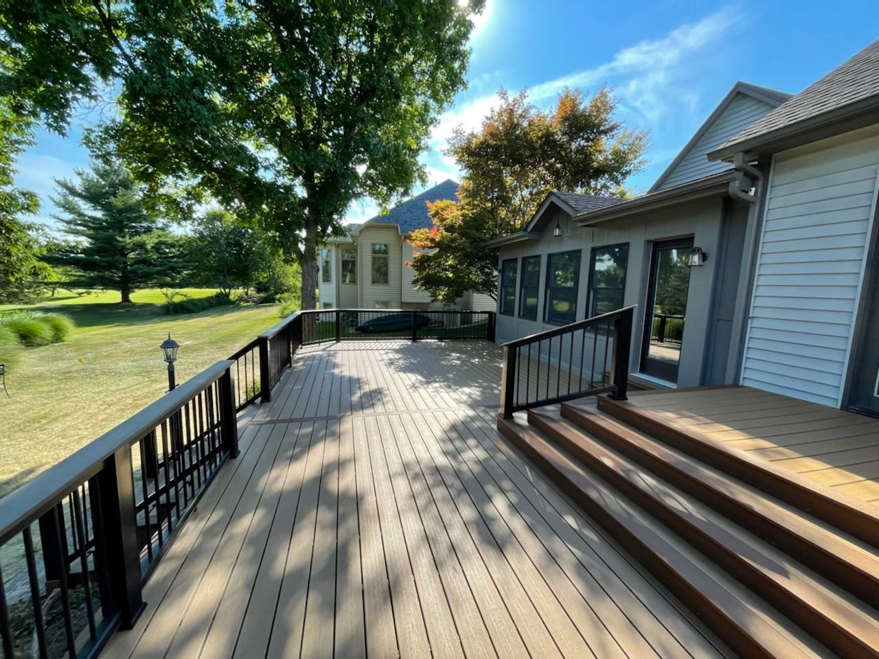 Composite deck with black railing, steps, and attached enclosed porch on a sunny day.