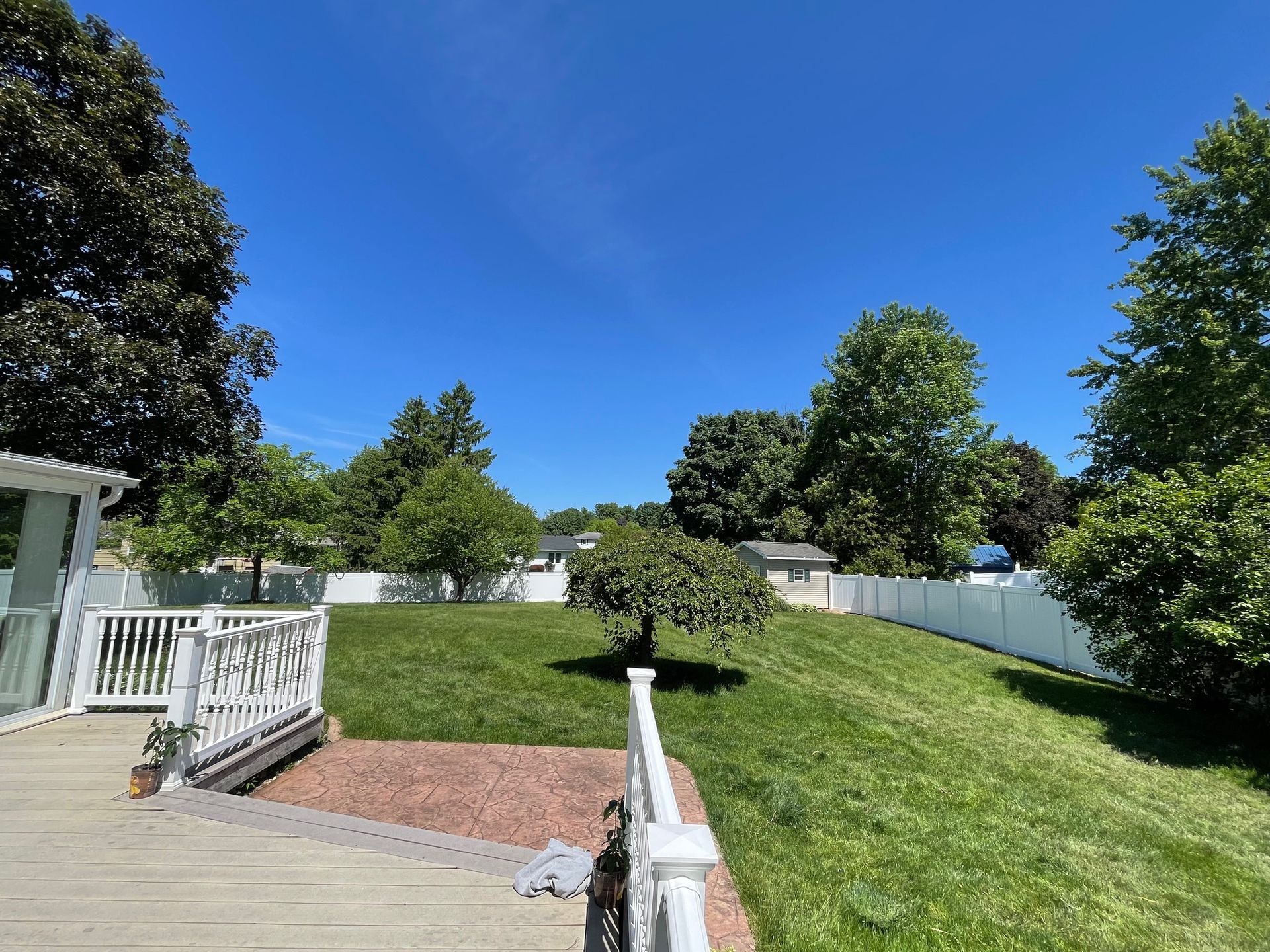 A lush green yard with a white fence and a deck.