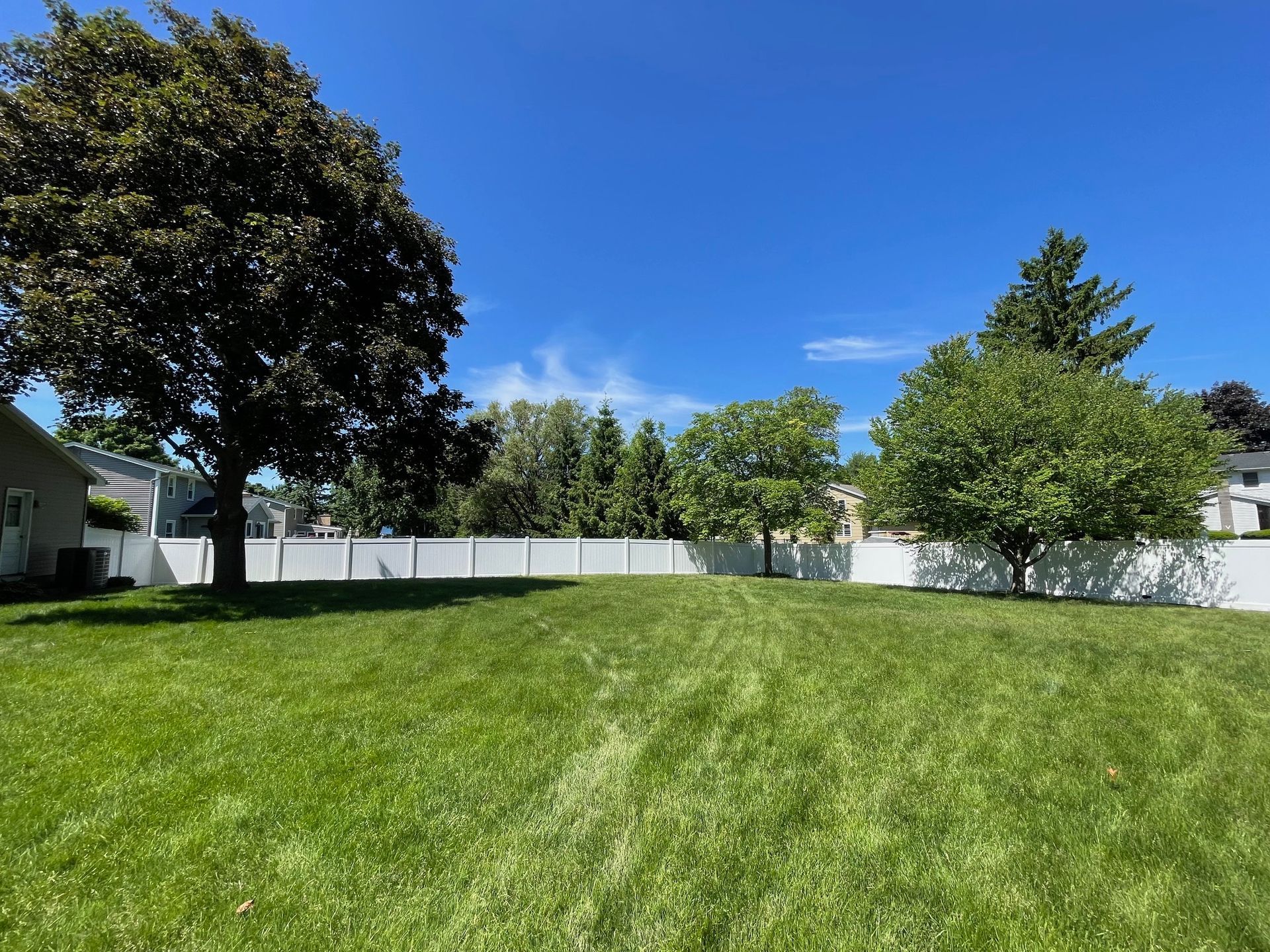A large lush green yard with a white fence and trees.