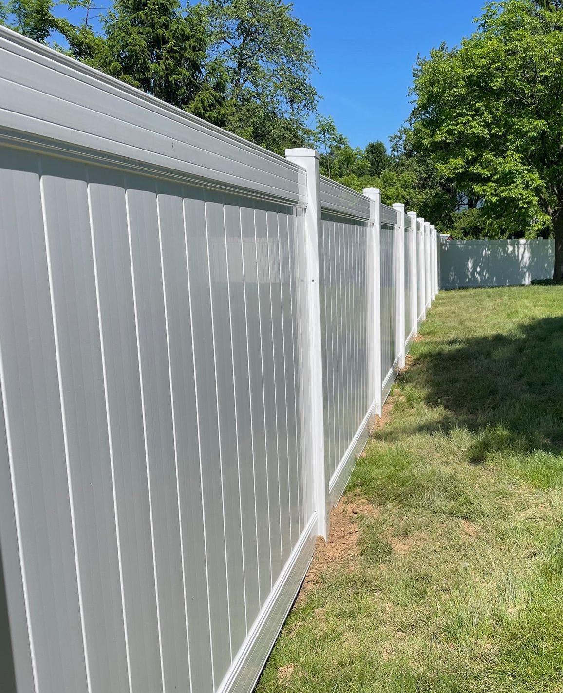 White vinyl fence along a grassy yard under blue sky and trees