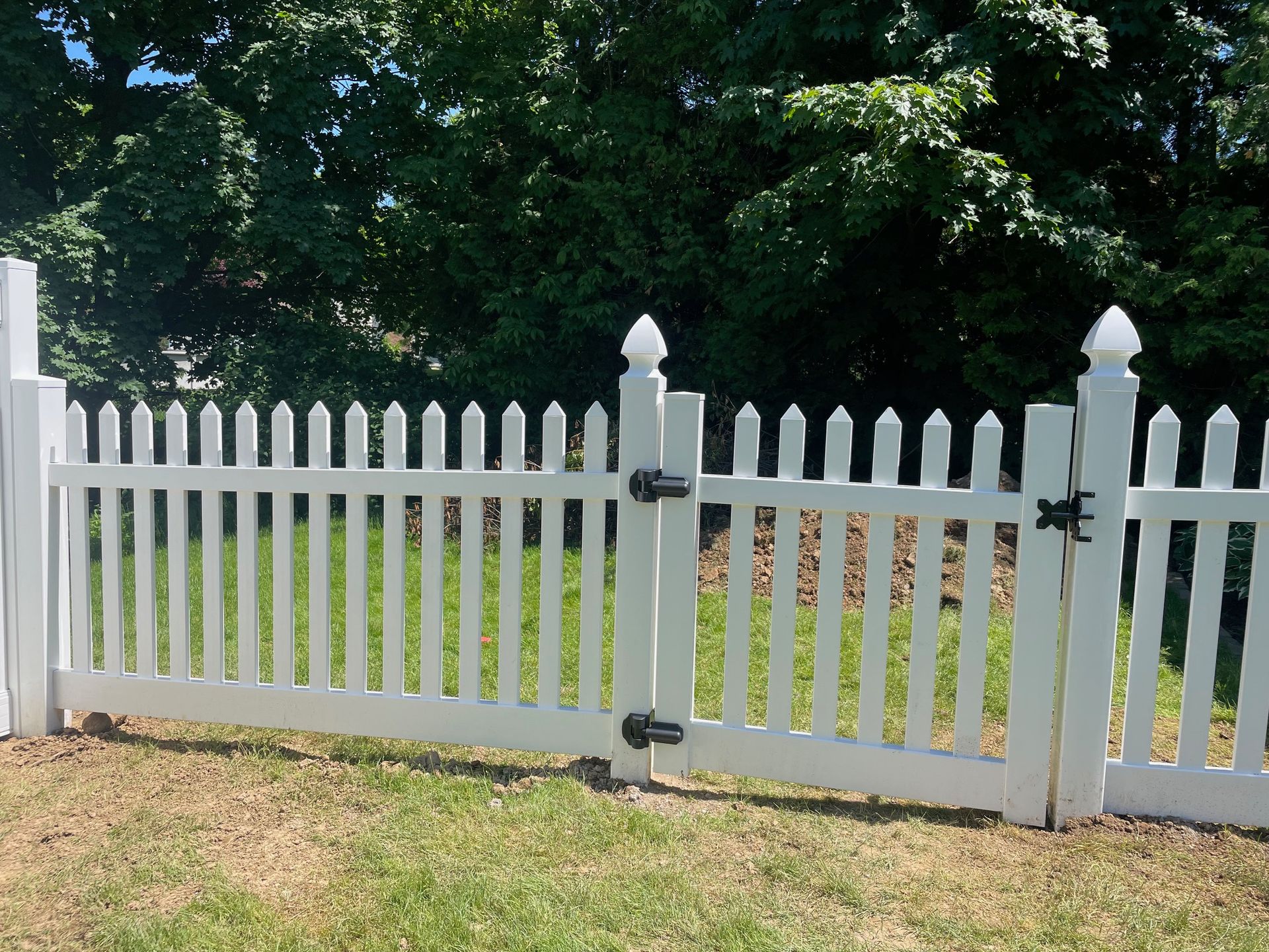 A white picket fence is surrounded by grass and trees