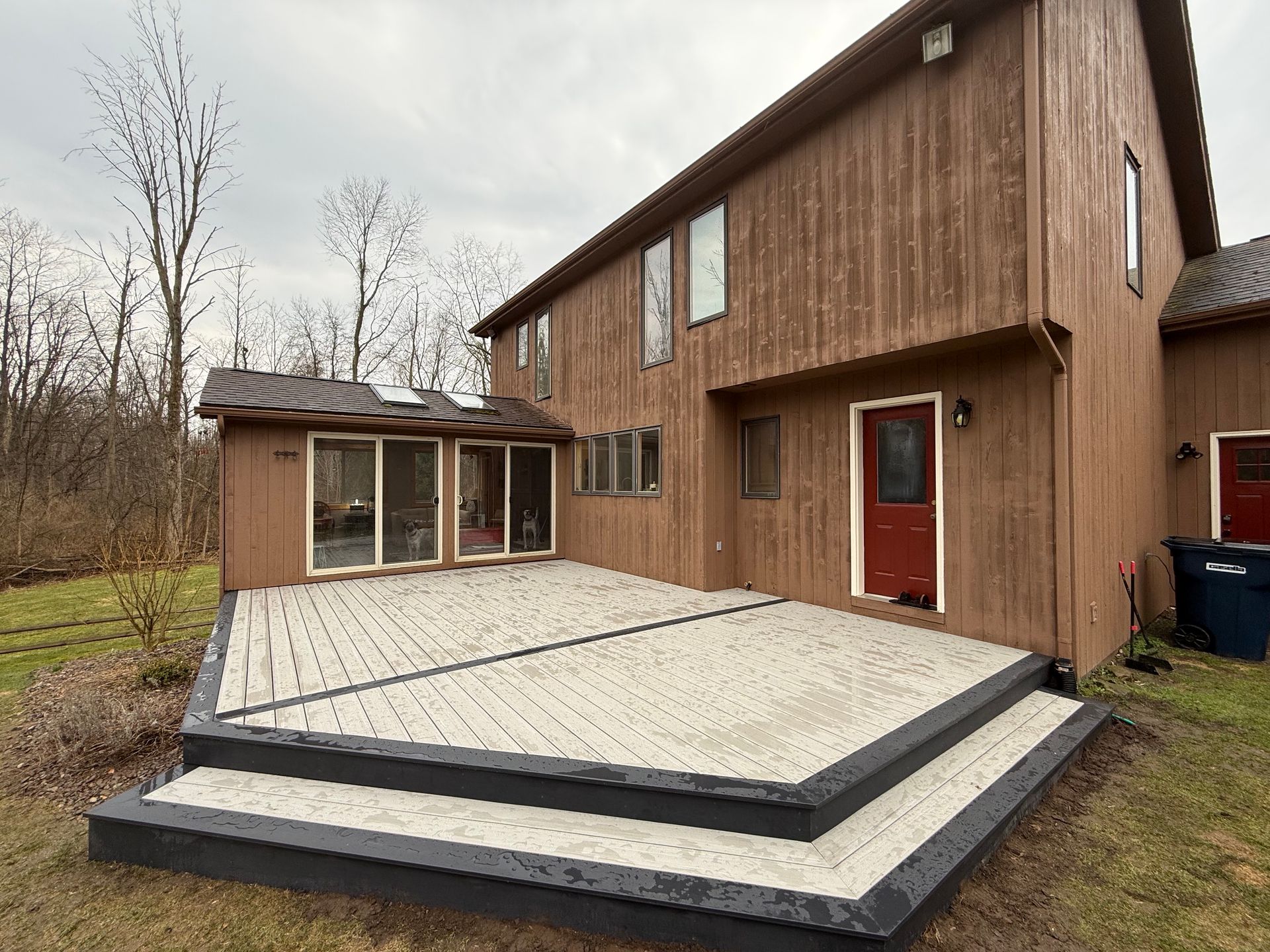 Wooden house deck under construction with light gray composite boards and dark trim steps