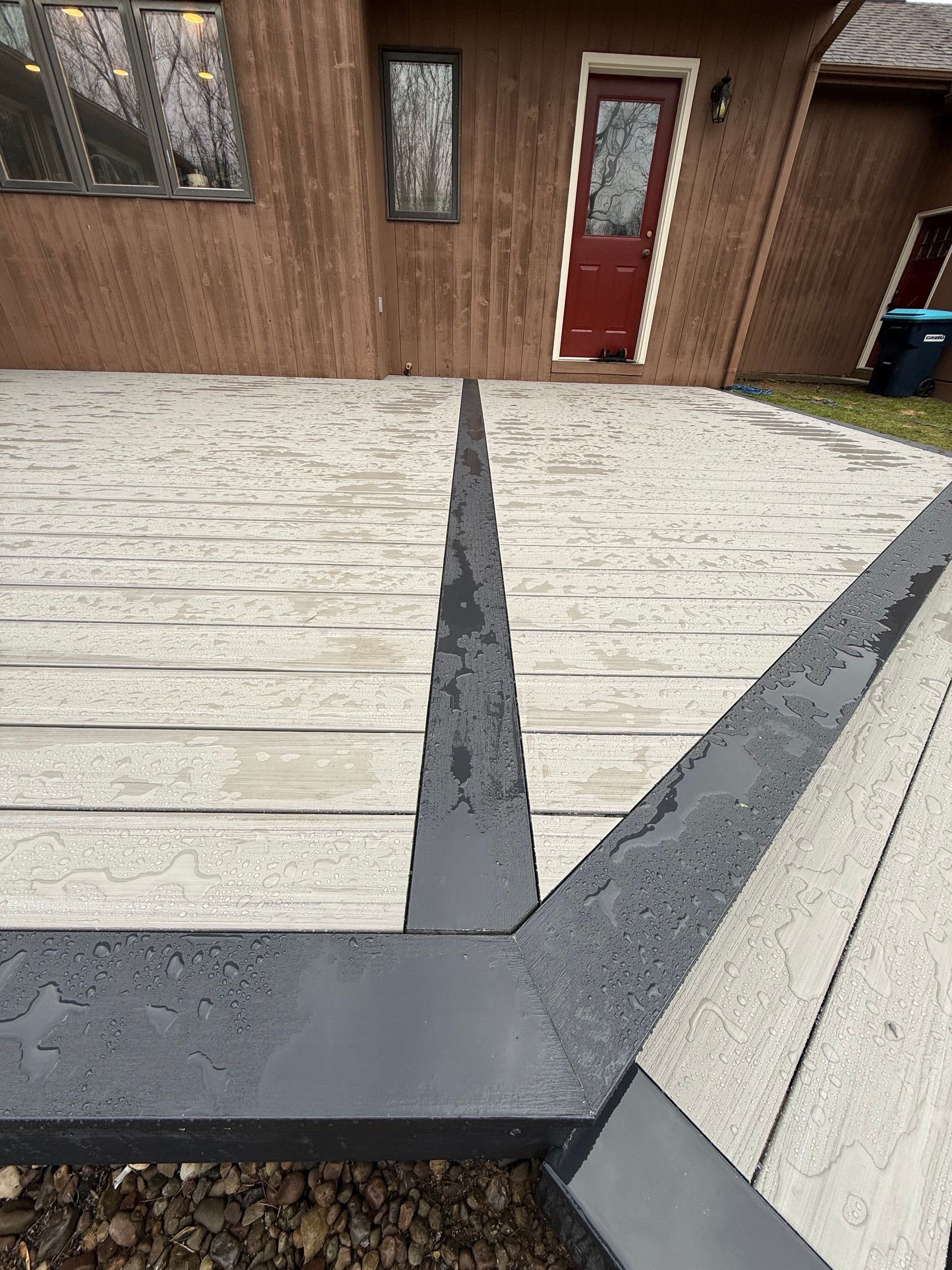 Wooden deck with gray concrete inlays and a red door on a brown building exterior.