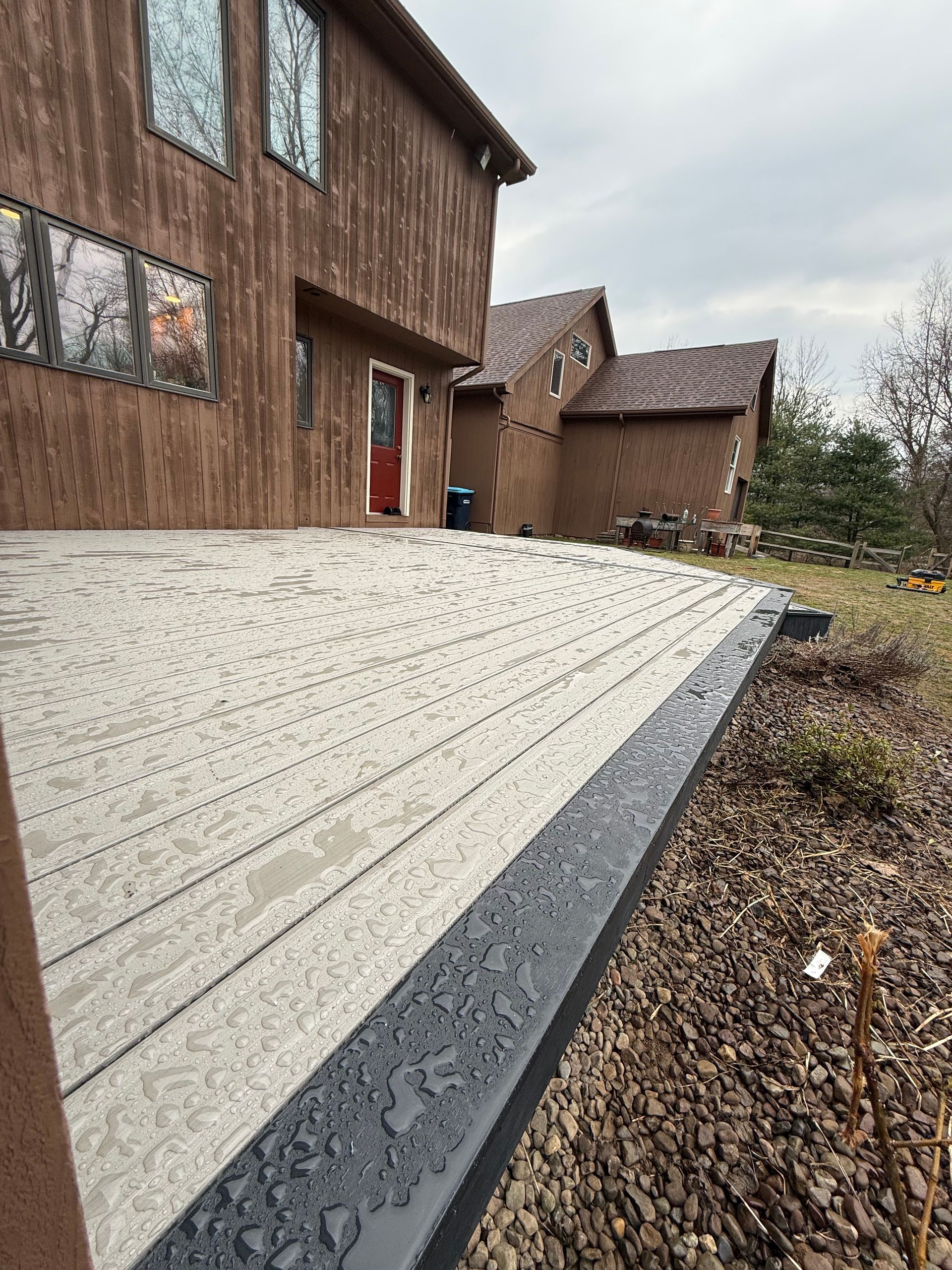 Stone patio beside a brown house, with a gravel border and overcast sky.