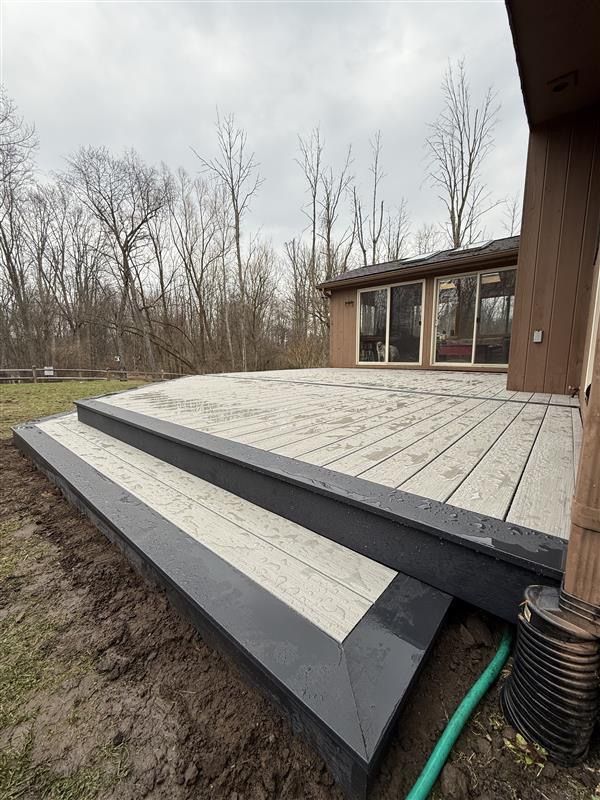 Outdoor wooden deck with wide steps beside a house, viewed from a muddy yard.