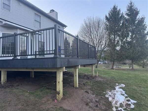 Raised wooden deck with black railing beside a house, overlooking a muddy yard with patches of snow.